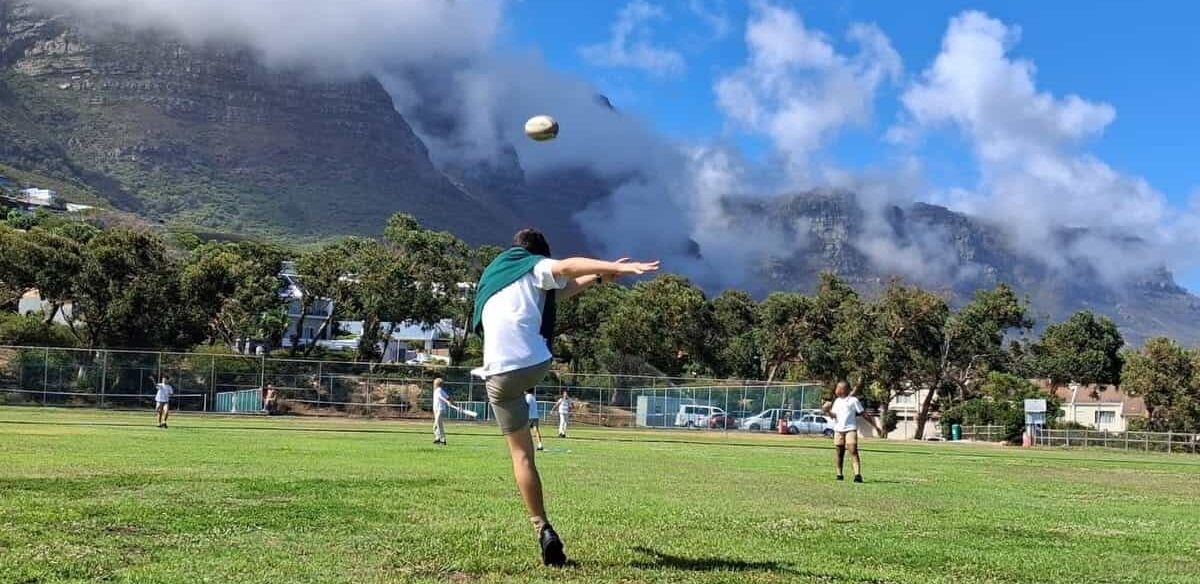 A learner kicking a rugby ball on the school field beneath the mountains