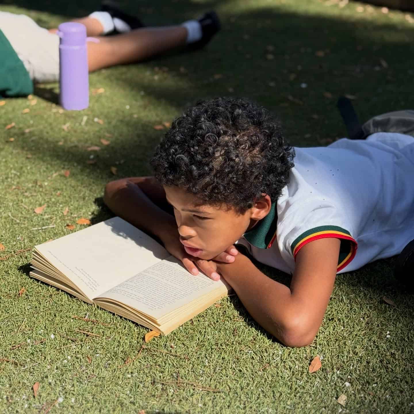 A learner reading a book while lying on the grass